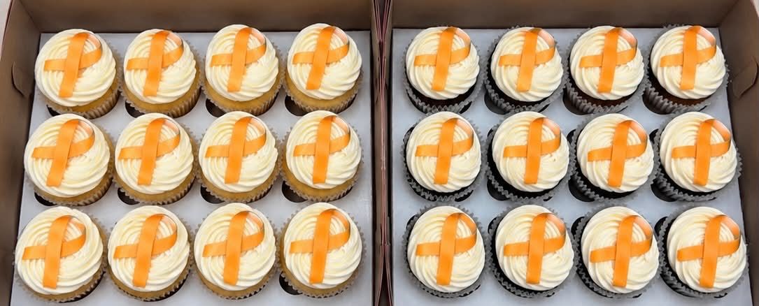 Two boxes of cupcakes topped with orange awareness ribbons