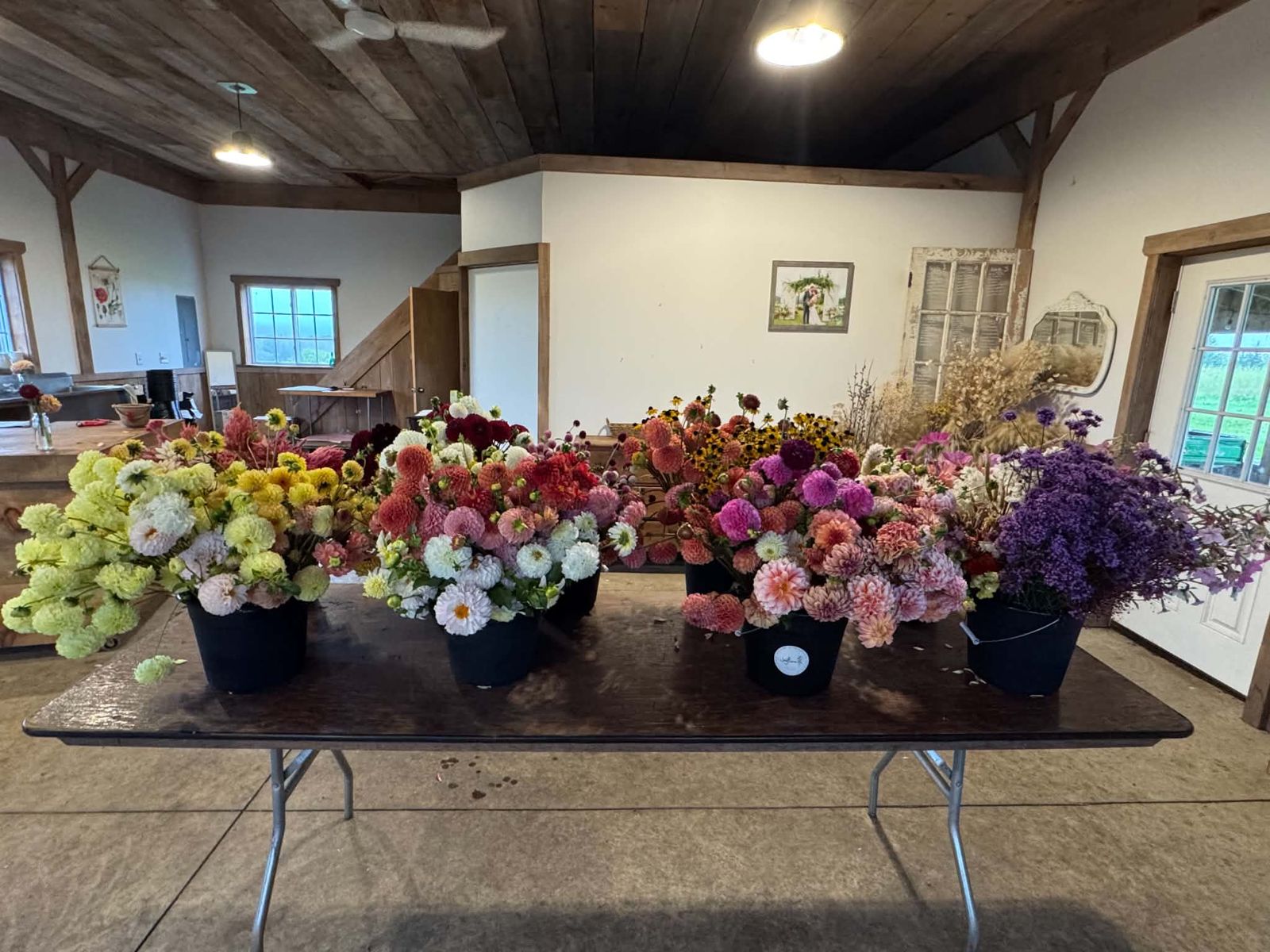 Buckets of fresh-cut dahlias lined up on a farm table before the Bloom Bar