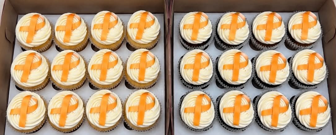 Two boxes of cupcakes topped with orange awareness ribbons