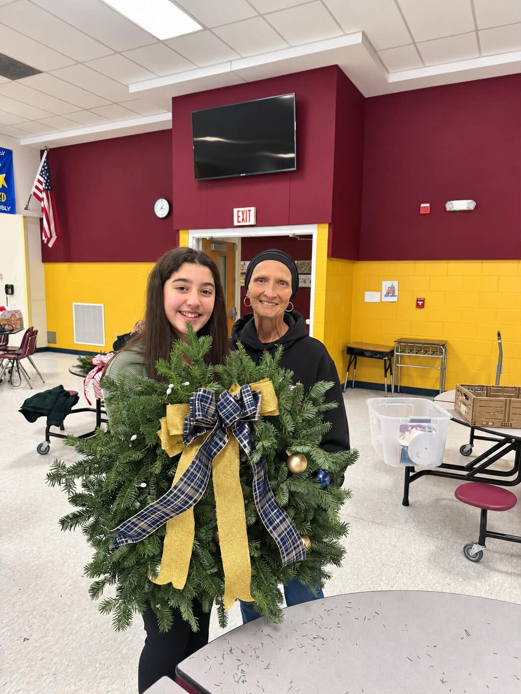 A volunteer and a young helper holding a blue and gold wreath