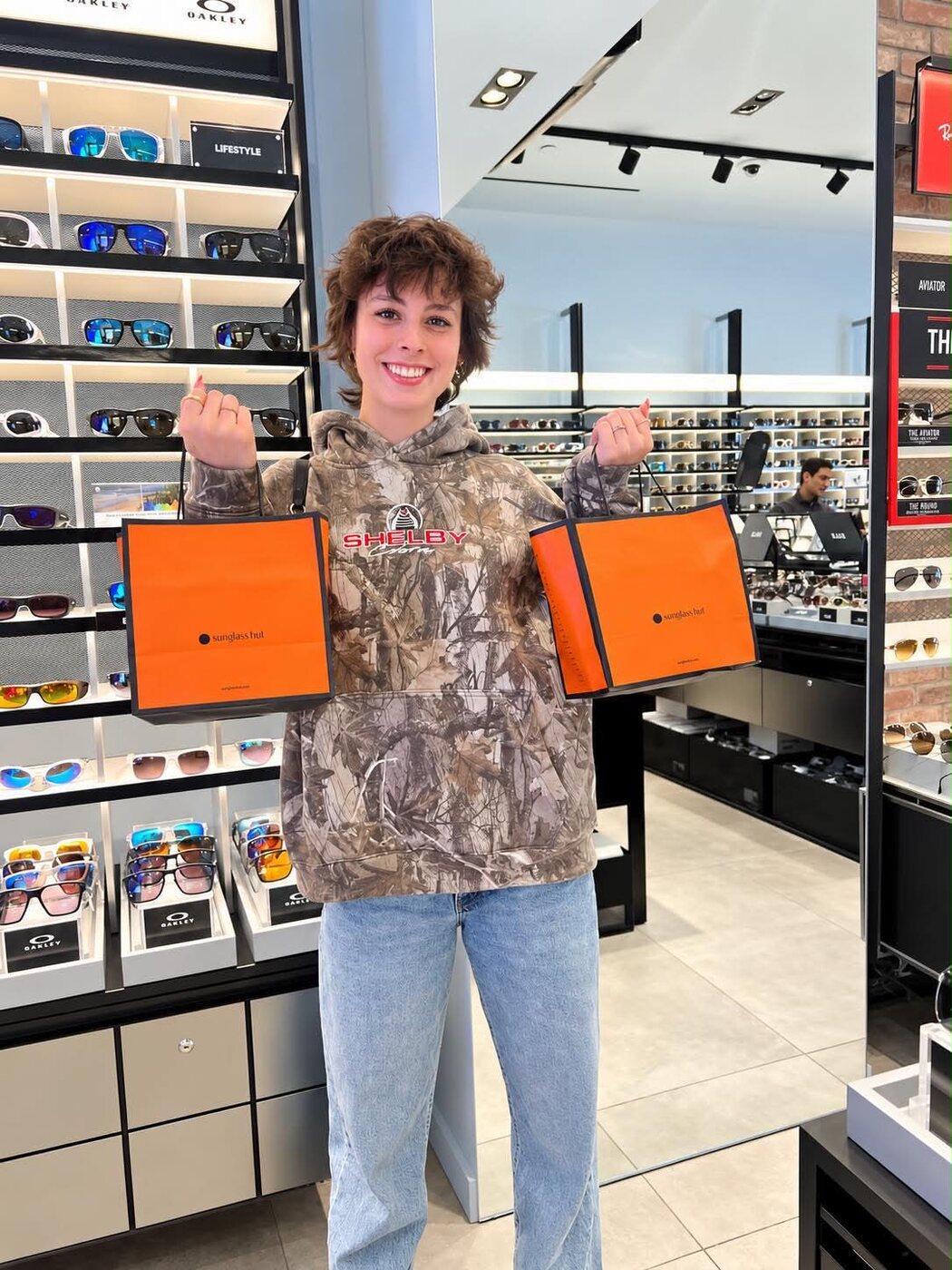 Annika smiling in a sunglasses shop holding two orange gift bags