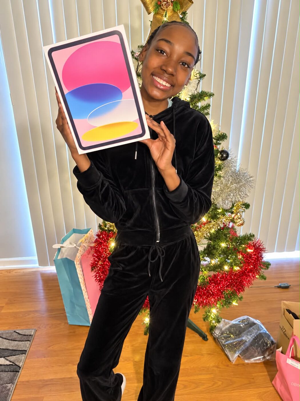 Arianna holding the pink iPad she had been wishing for beside a Christmas tree