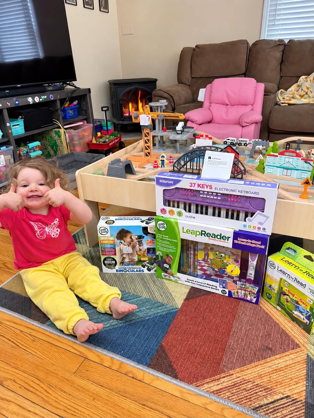 Octavia sitting with her new LeapFrog toys and electronic keyboard, giving two thumbs up